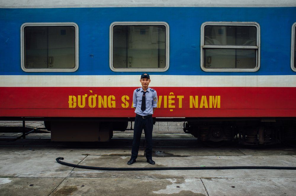 A man is standing in front of a blue and red train.