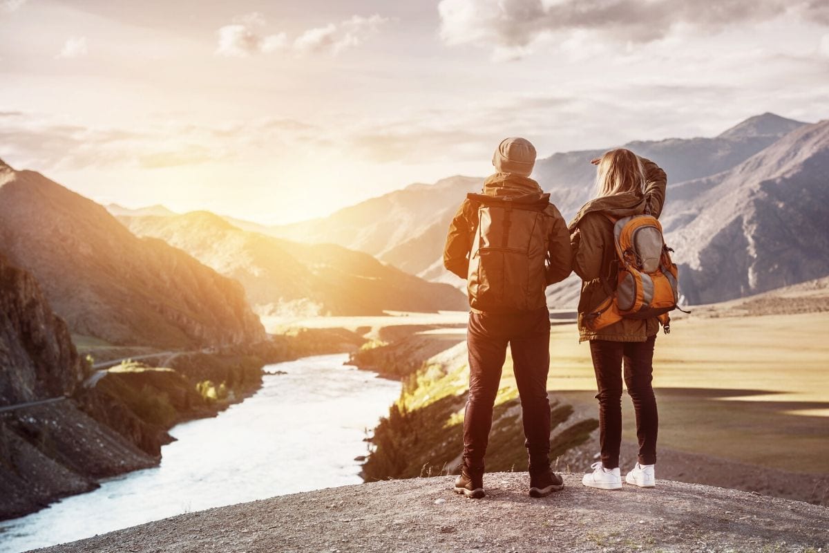 A man and a woman are standing on top of a mountain looking at a river.