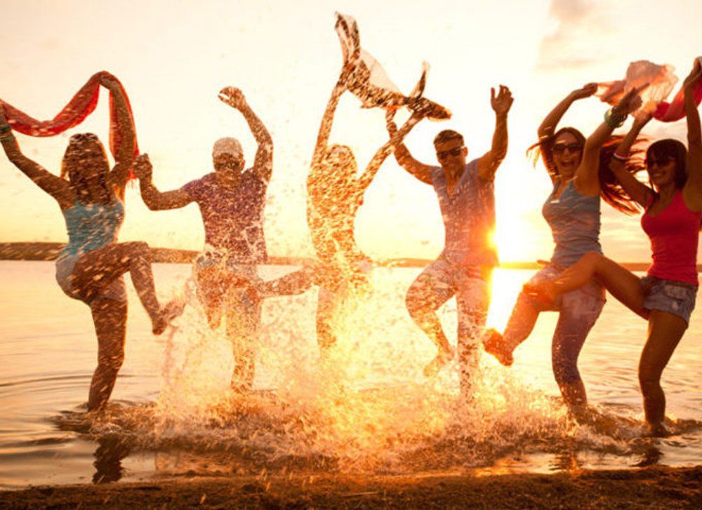 A group of people are jumping into the water on a beach at sunset.