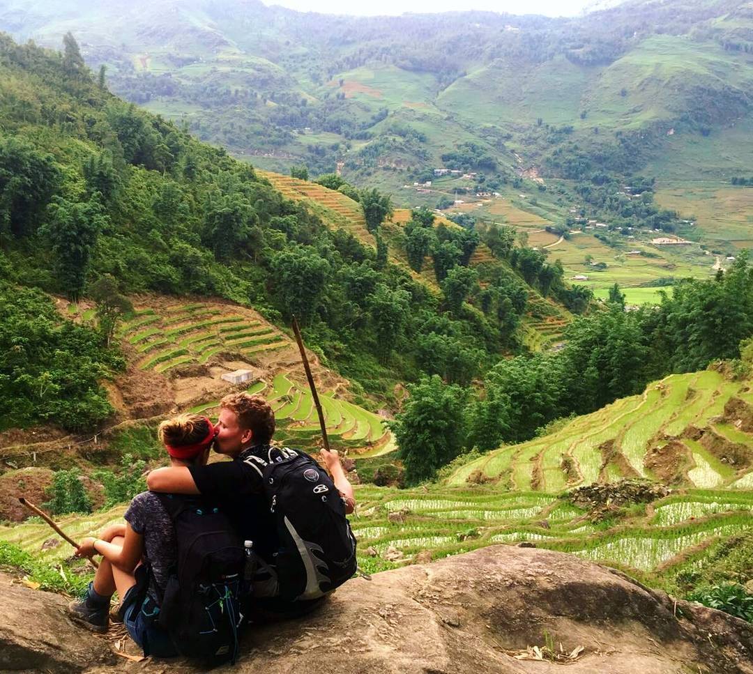 A man and woman are sitting on a rock overlooking a valley.