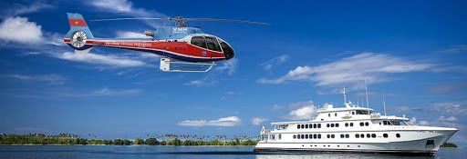 A helicopter is flying over a boat in the water.