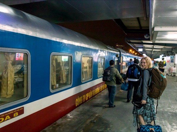 A woman with a backpack is walking towards a blue and white train.