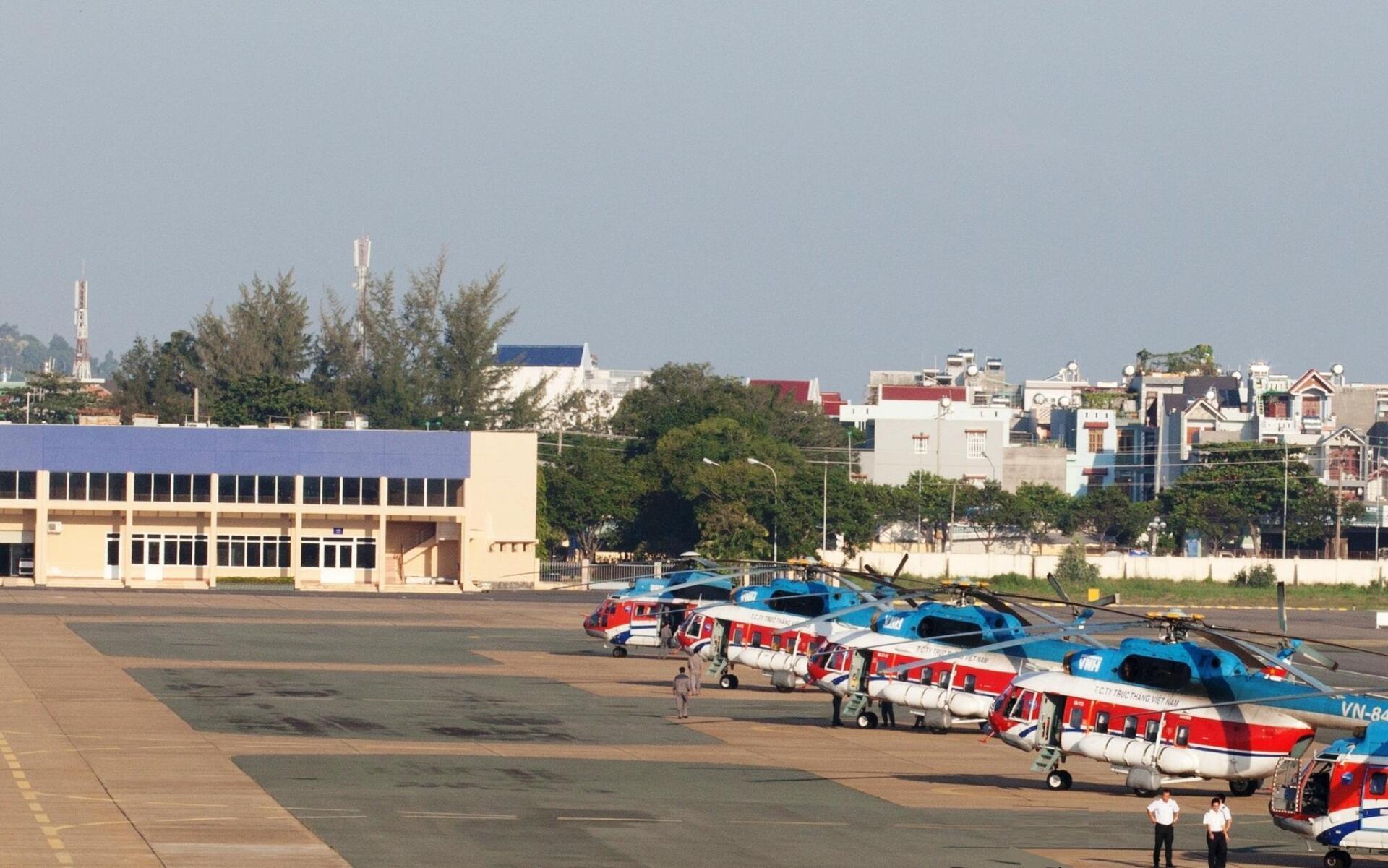 A row of helicopters are parked on a runway in front of a building.