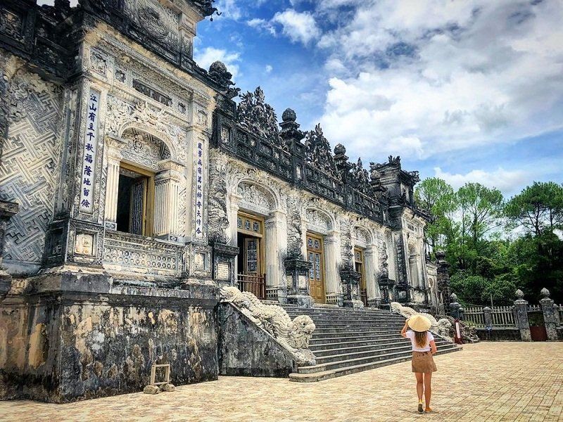 A woman in a conical hat is standing in front of a large building.