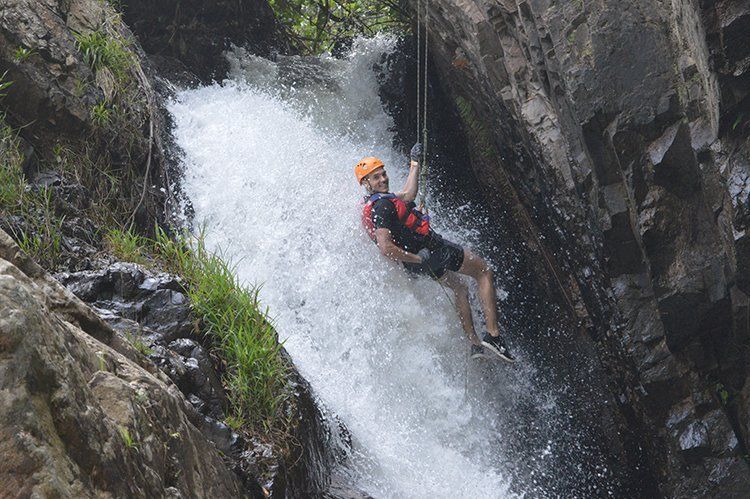A man is hanging from a rope in a waterfall.