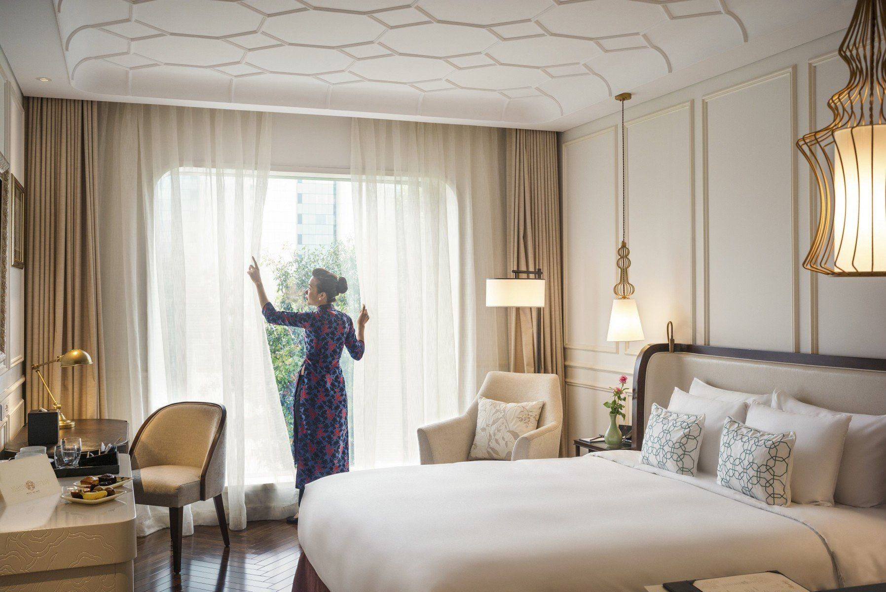 A woman is standing in a hotel room looking out of a window.
