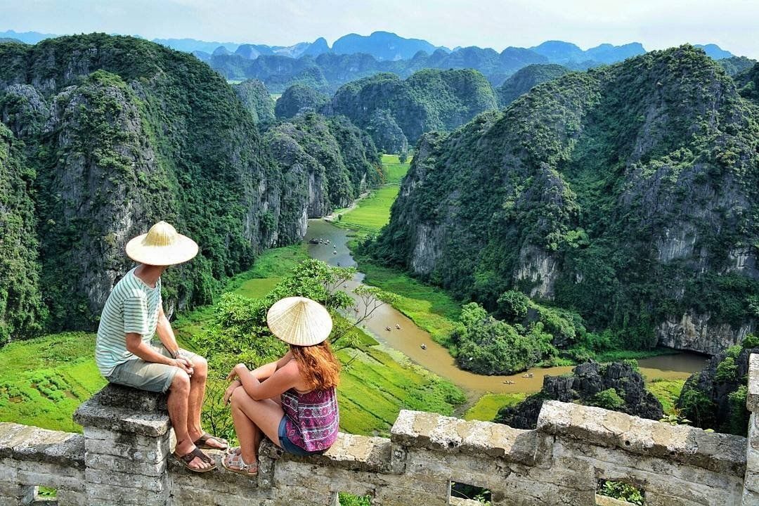 A man and a woman are sitting on a wall overlooking a valley.