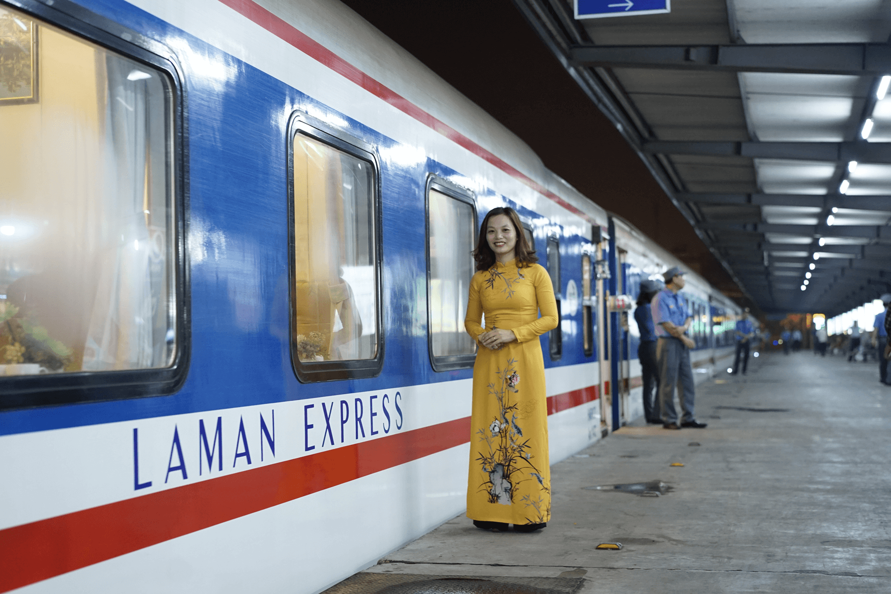 A woman in a yellow dress is standing next to a blue and white train.