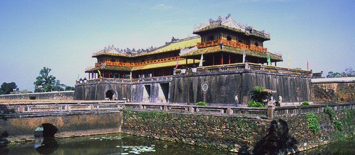 A large building is sitting on top of a hill next to a body of water.