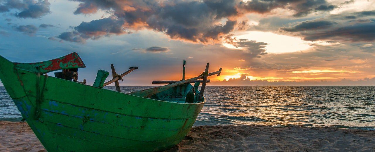 A green boat is sitting on the beach at sunset.