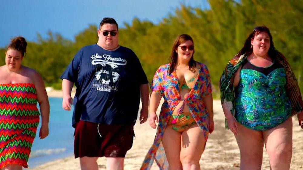 A group of overweight people are walking on a beach.