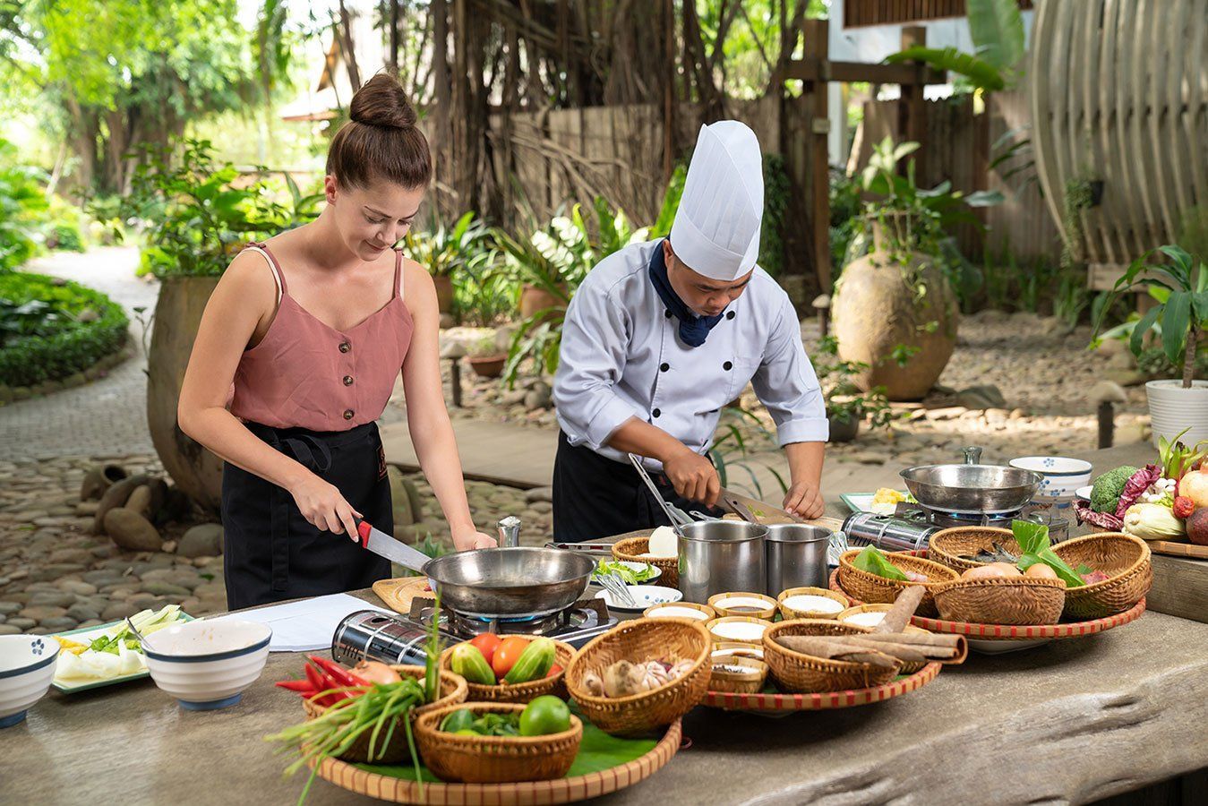 A woman is standing next to a chef preparing food on a table.