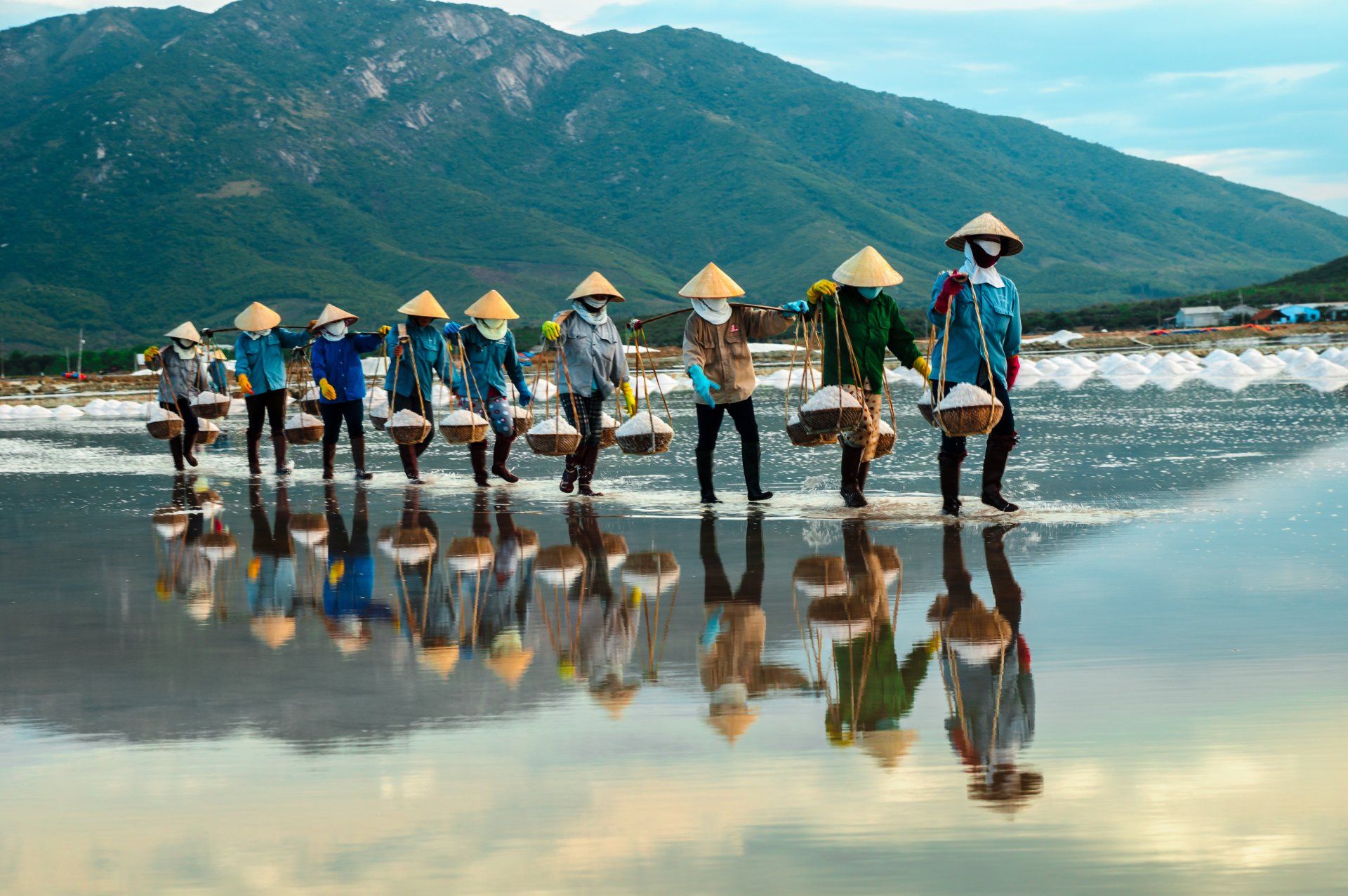 A group of women are walking across a body of water carrying baskets of salt.