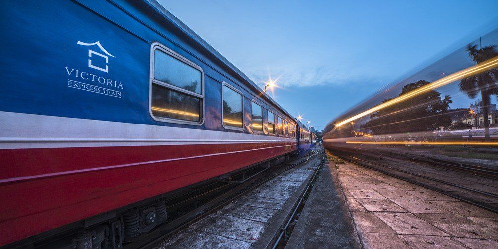 A blue and red train is parked on the tracks at a train station.