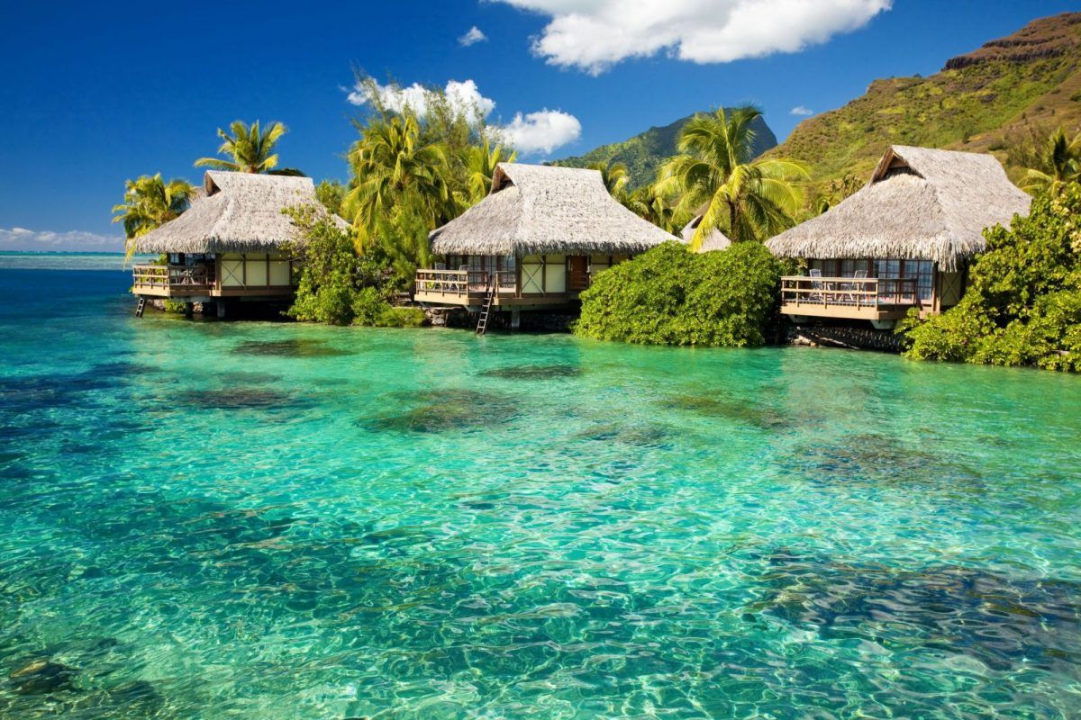 A row of thatched huts on a small island in the middle of the ocean.