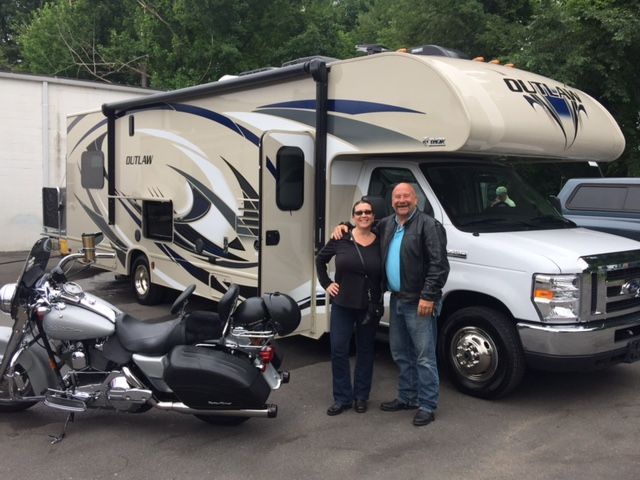 A man and woman standing in front of a rv and a motorcycle