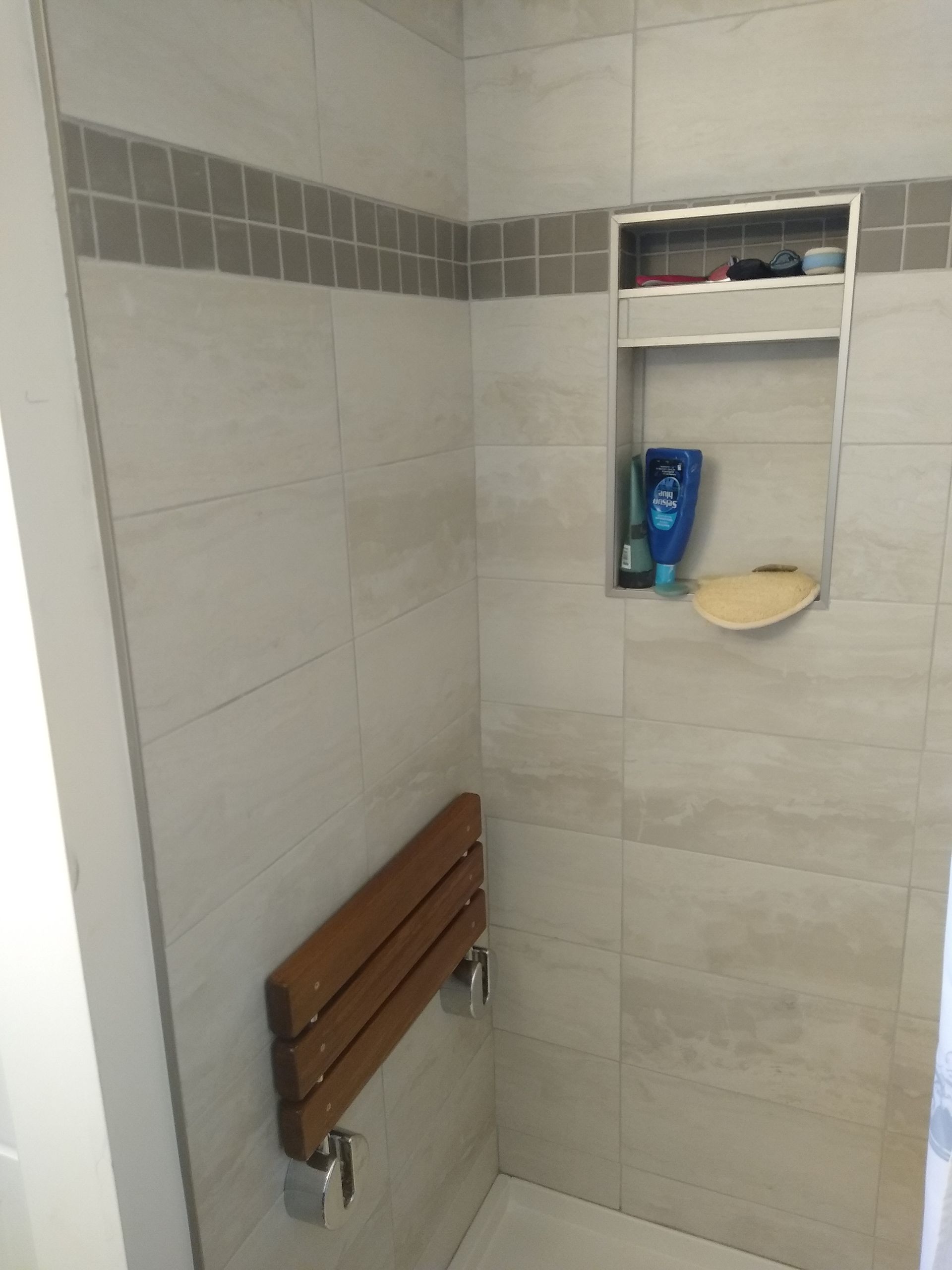 A shower with a wooden bench and a shelf.