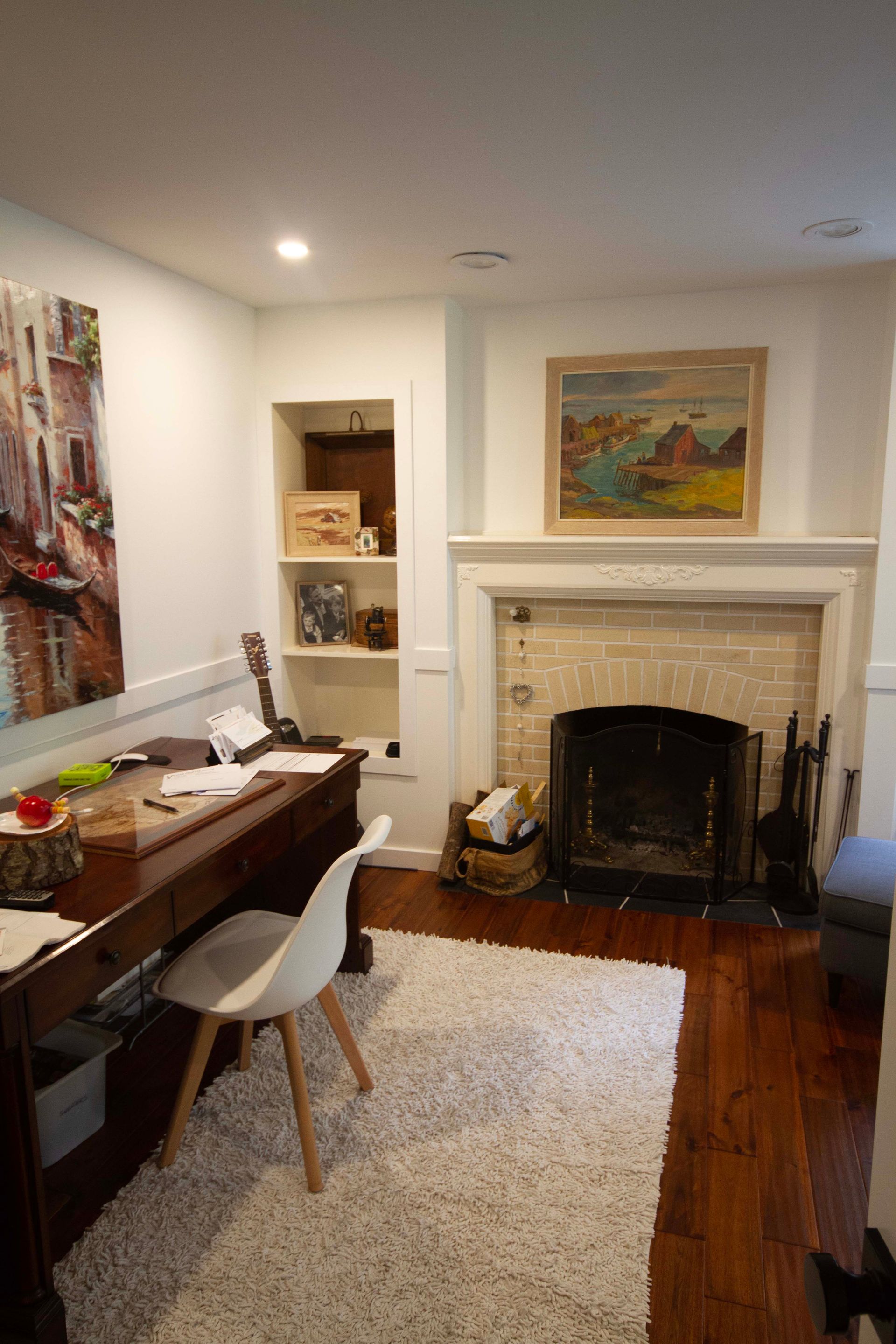 A living room with a fireplace , desk , chair and painting on the wall.