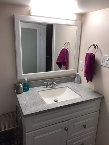 A bathroom with a sink , mirror and purple towels hanging on the wall.