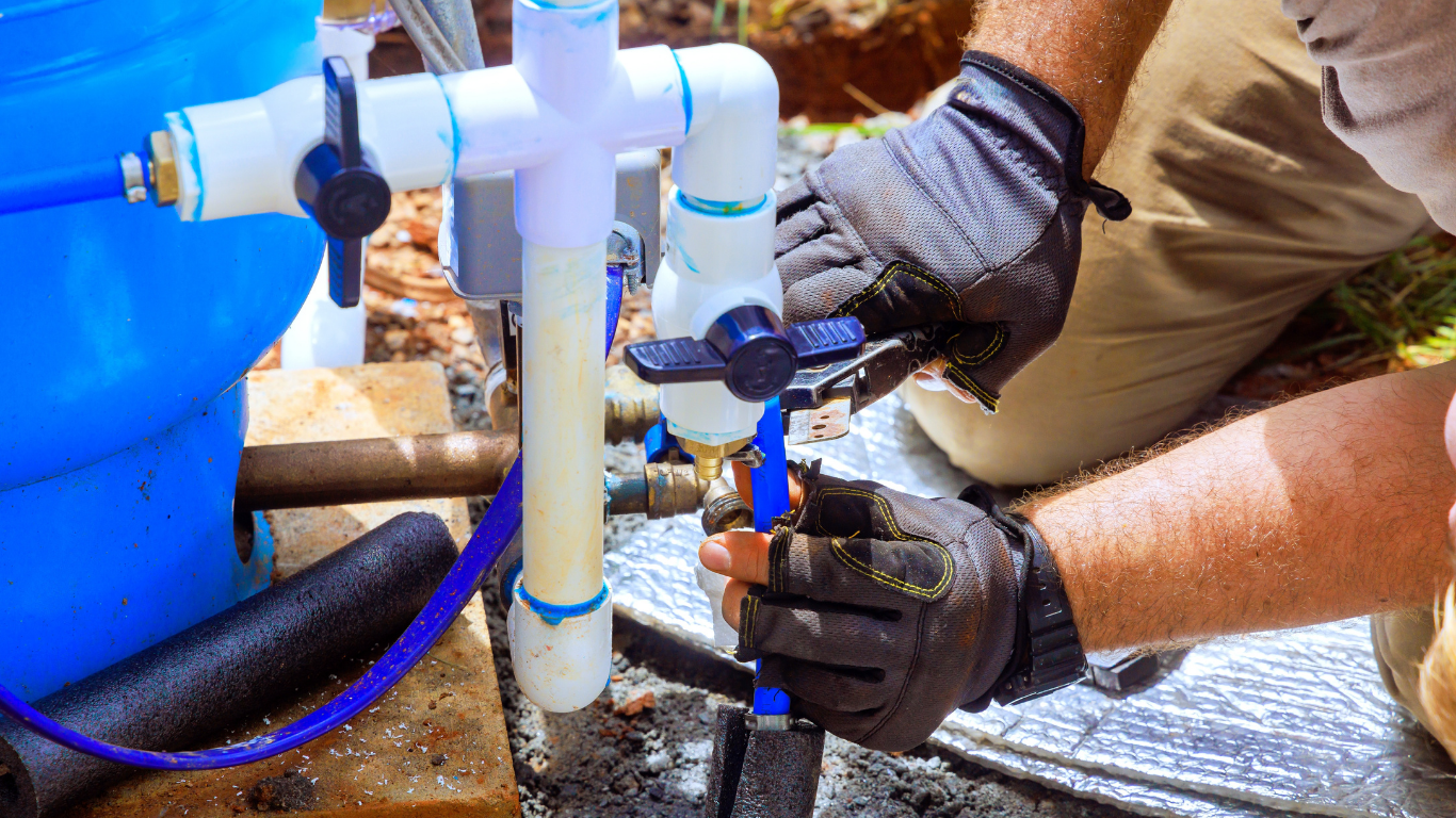 A person wearing gloves, working on PVC pipes, blue water tank in the background.