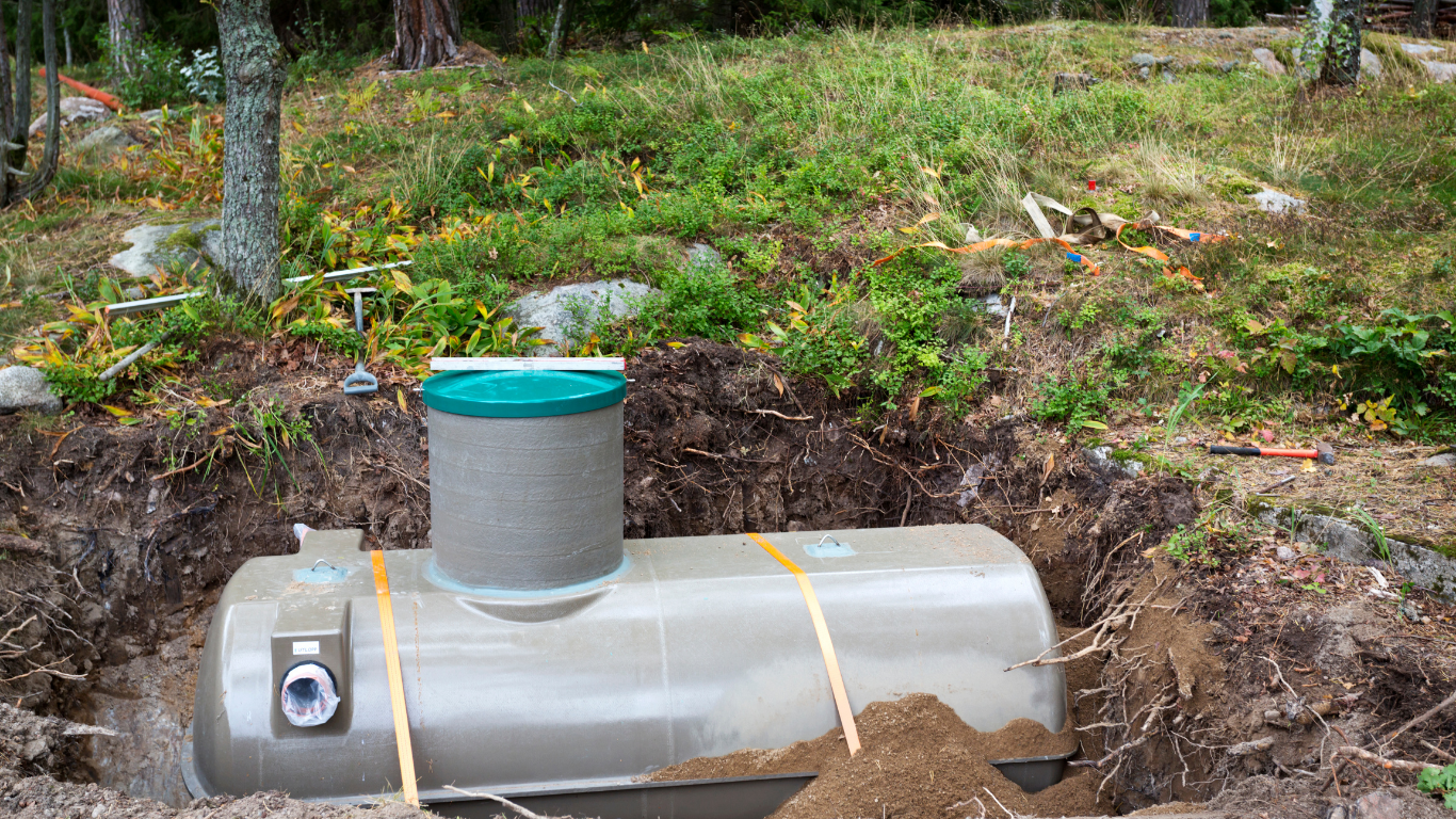 Septic tank installation in progress outdoors; tank in excavated soil with concrete riser.