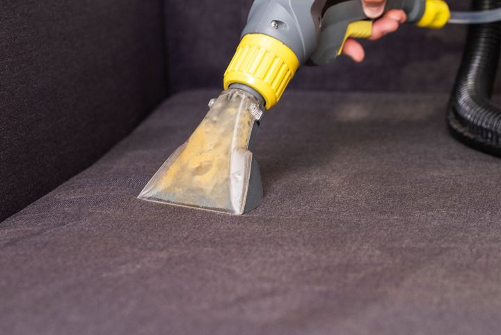 A person is cleaning a couch with a vacuum cleaner.