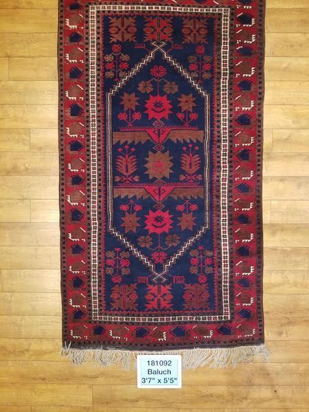 Blue and red patterned rug with floral and geometric designs, fringed edges on wooden floor.