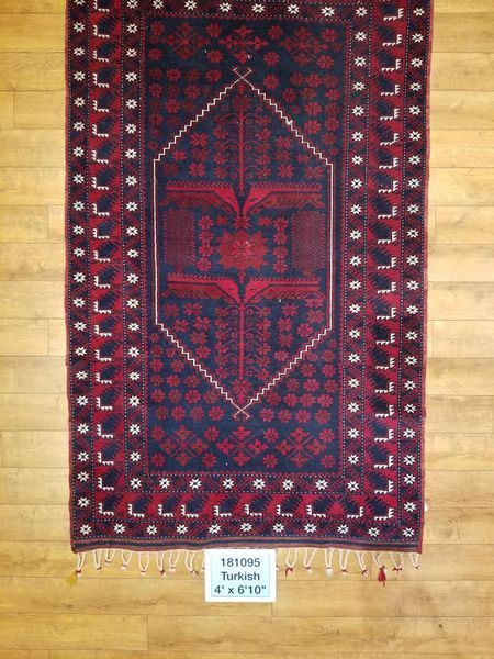 Dark blue and red tribal rug on wood floor; central stylized floral design, geometric border.