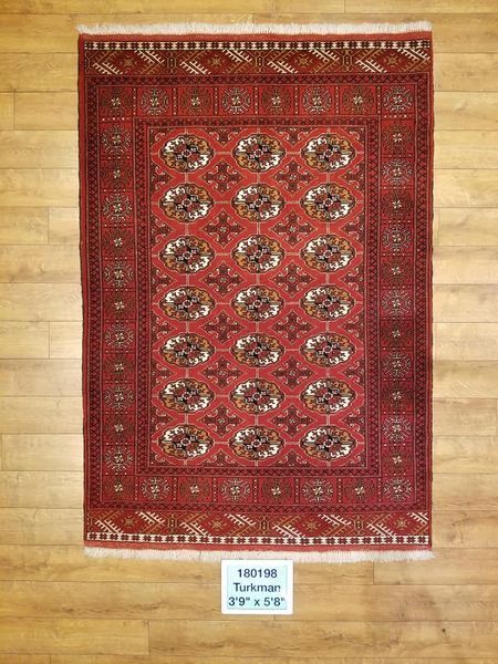 Red and brown rectangular rug with repeating floral patterns and border, resting on a wood floor.