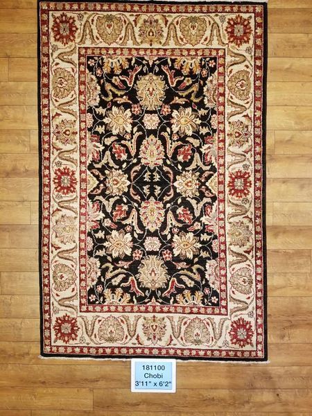 An ornate black rug with a floral pattern and a beige border. It rests on a wooden floor.