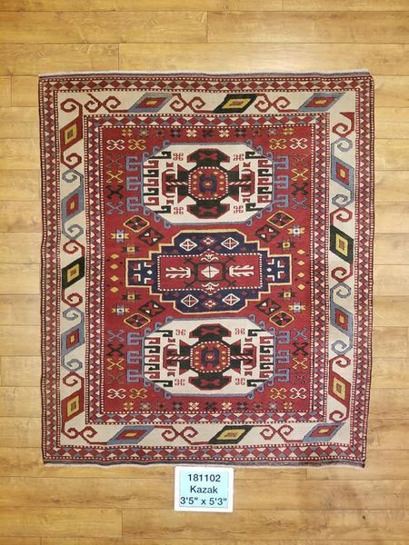 Red, cream, and blue rectangular rug with geometric designs on wooden floor.
