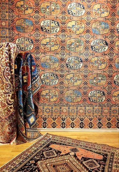 Carpets displayed on a wall and floor, various patterns and colors including reds, blues, and golds.