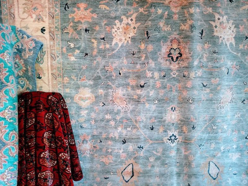 Various patterned rugs with a red floral patterned textile hanging in front of them.