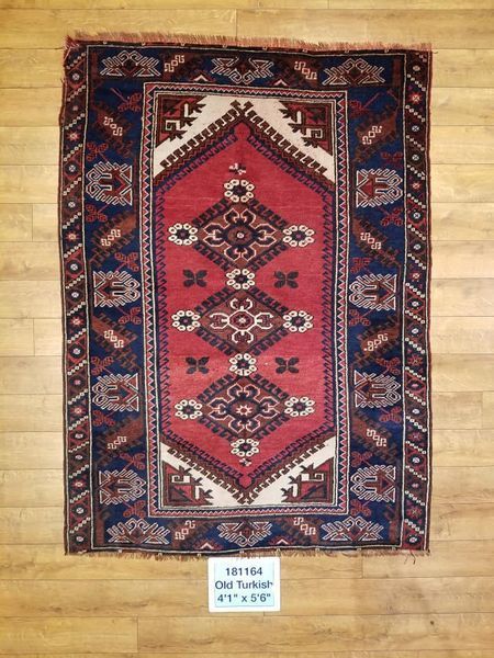 Red and blue antique Turkish rug with central diamond design and geometric border on wood floor.