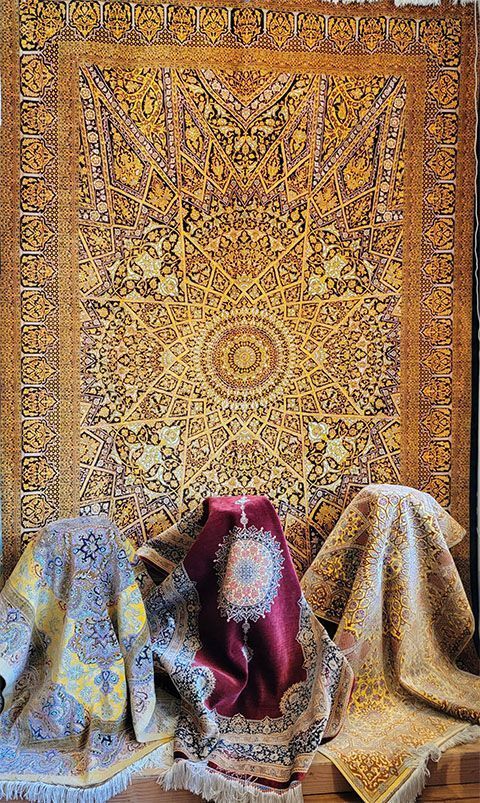 Large, ornate rug with gold and black patterns displayed, with three smaller rugs draped below.
