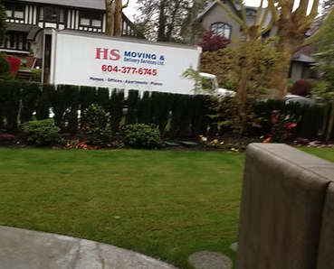 Moving truck parked in front of a house, with a green lawn and hedge.