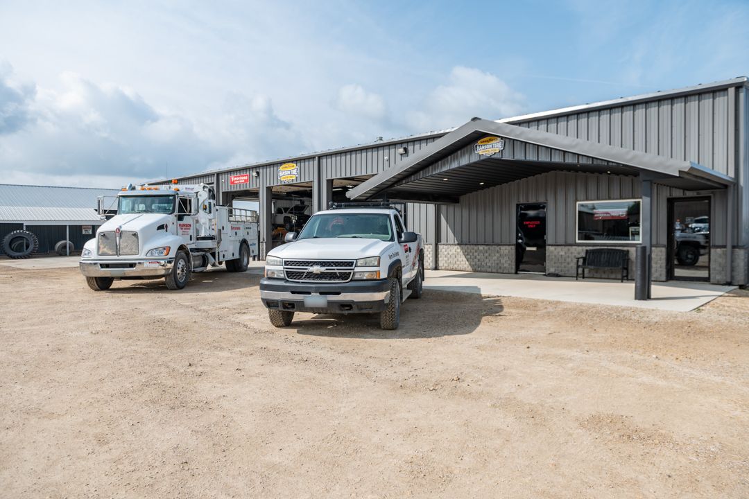 Exterior of a commercial building with a white truck, silver pickup, and gravel lot on a sunny day.