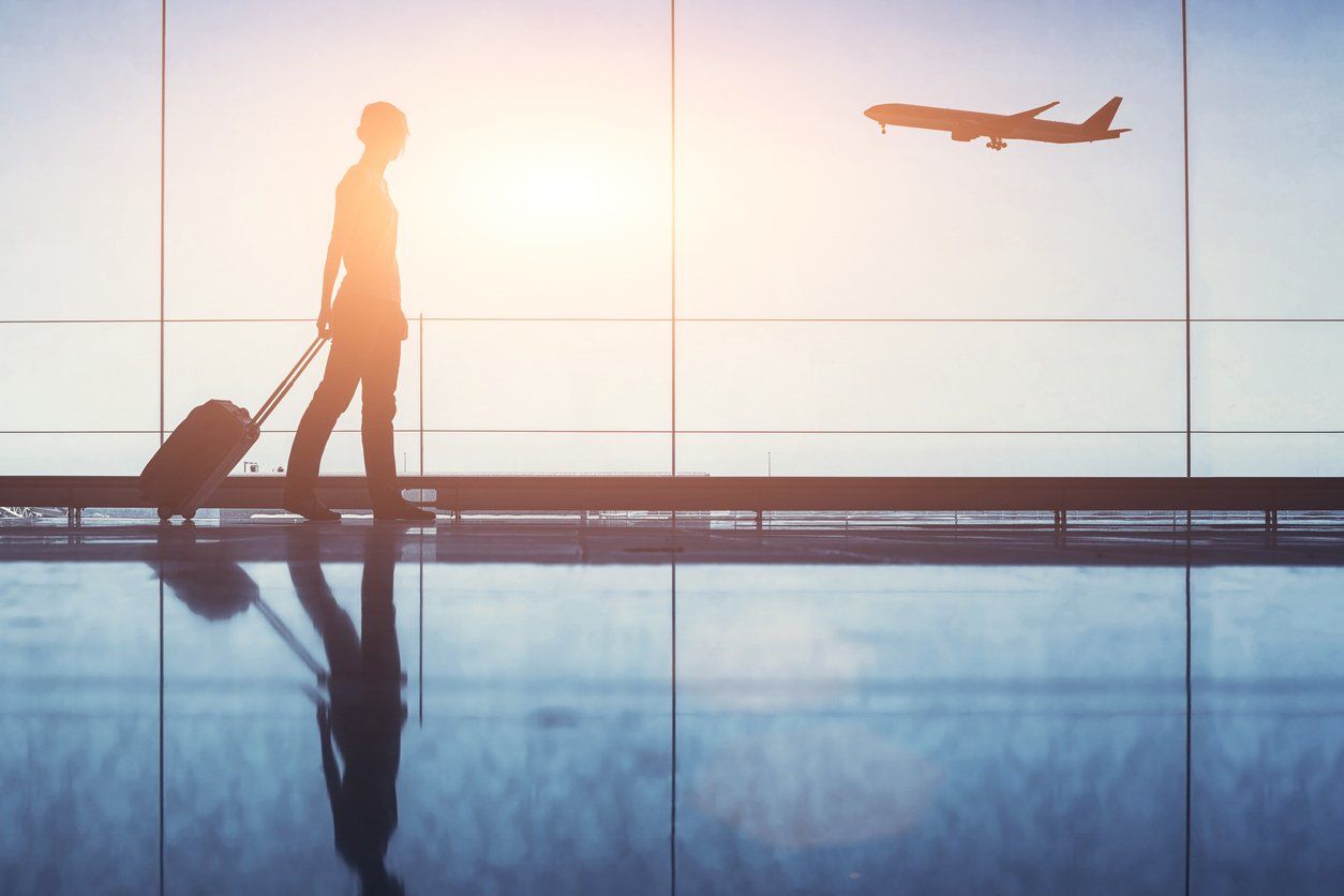 photo of a person walking through an airport with luggage and an airplane in the sky