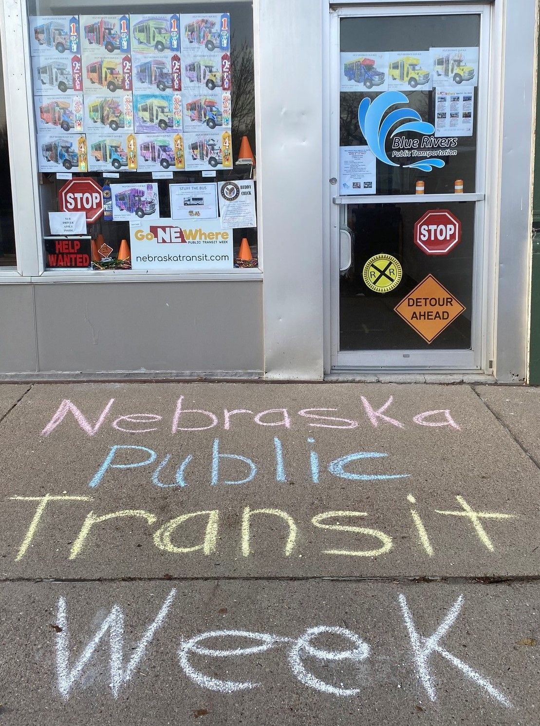 photo of office window with coloring contest pages hung up and sidewalk chalked with Nebraska Public Transit Week