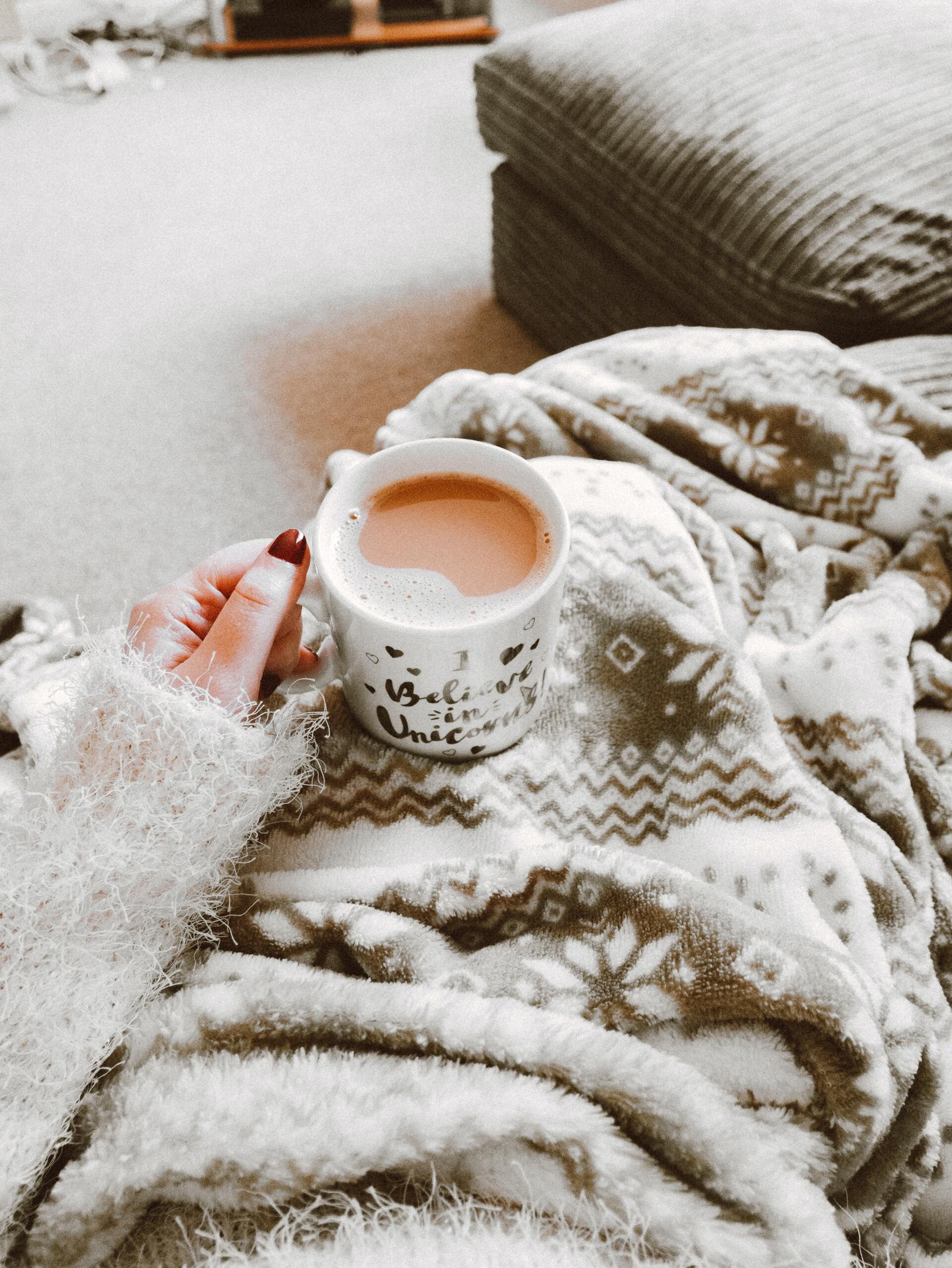 photo of a person wrapped in a blanket with a mug filled with a warm beverage