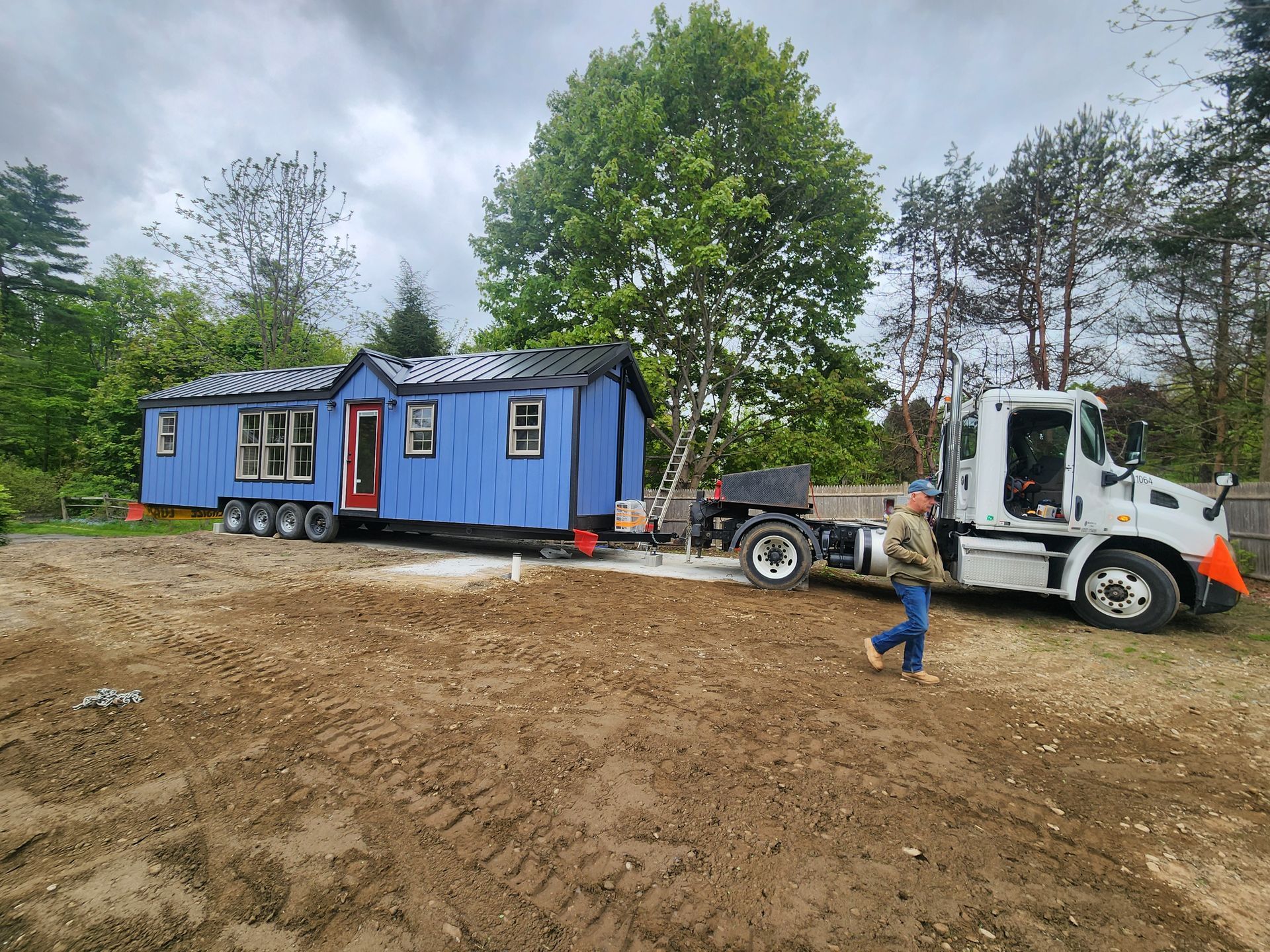 Yellow semi-truck transporting a modular home on a highway through a forest. A car follows.