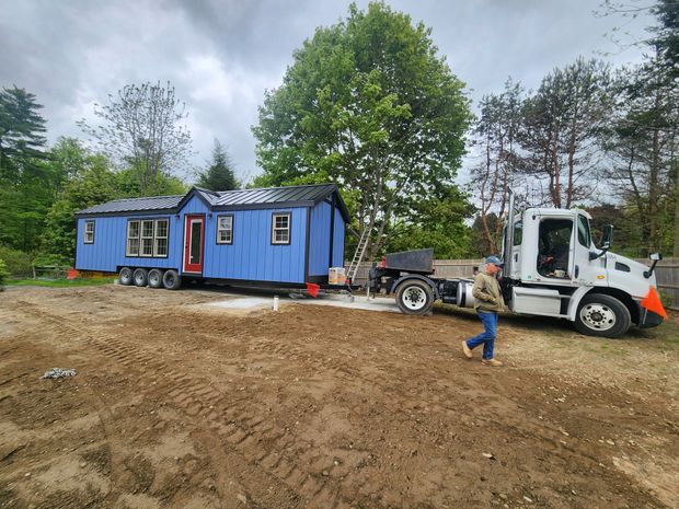 Yellow semi-truck transporting a modular home on a highway through a forest. A car follows.