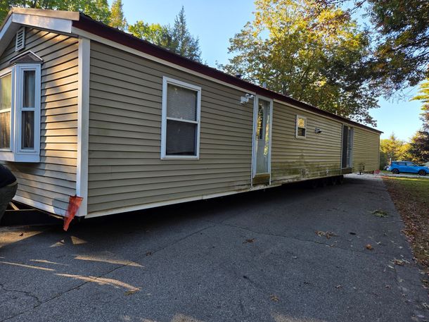 A tan manufactured home with white trim parked on a gravel lot during a sunny day.