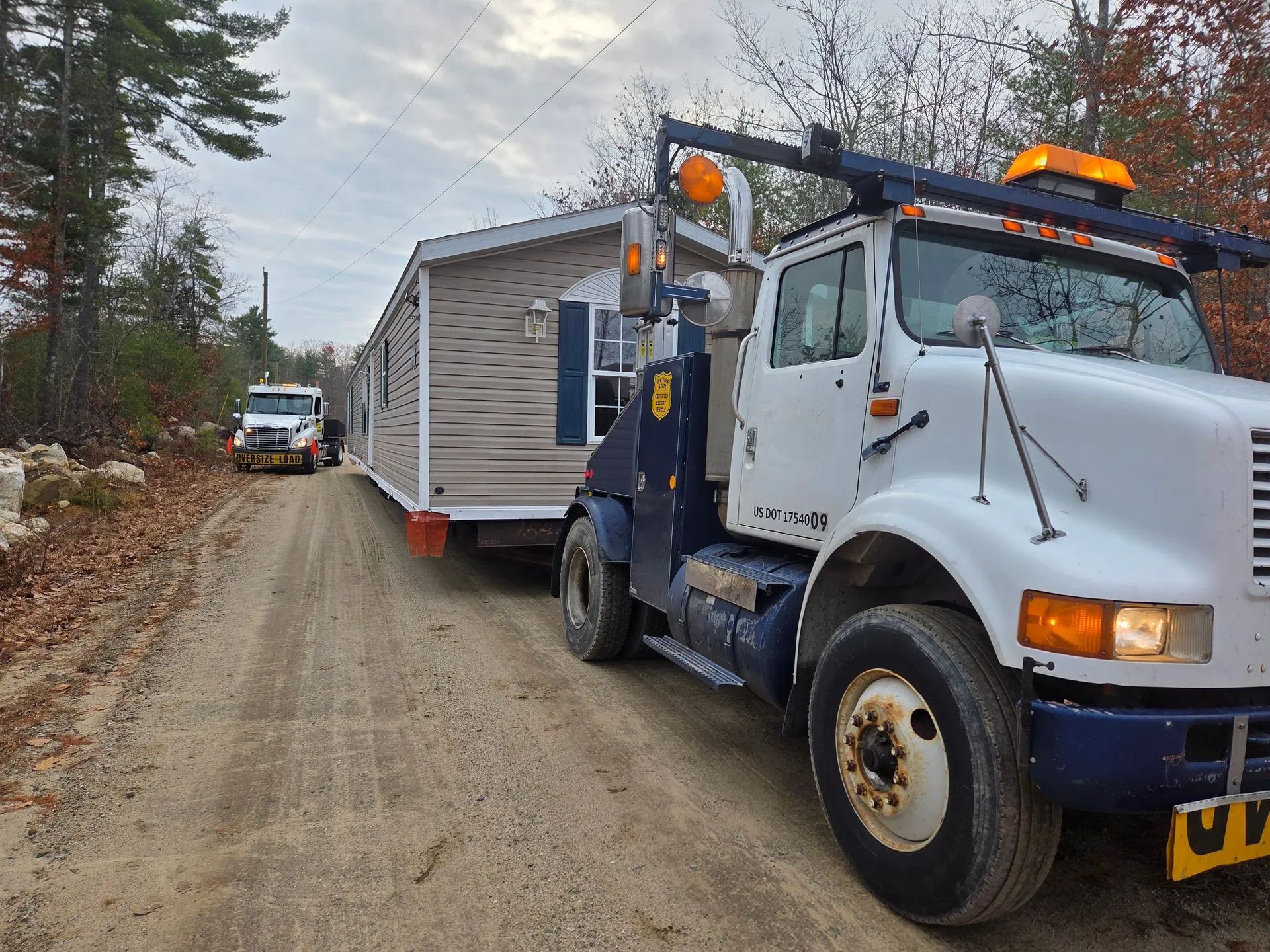 A white truck towing a mobile home on a dirt road lined with trees.