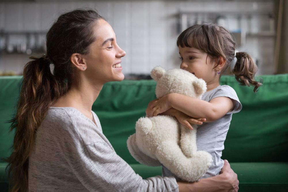 A Woman Is Holding A Teddy Bear In Her Arms While A Little Girl Looks On — Bradley J Bragg - Solicitor in Atherton, QLD