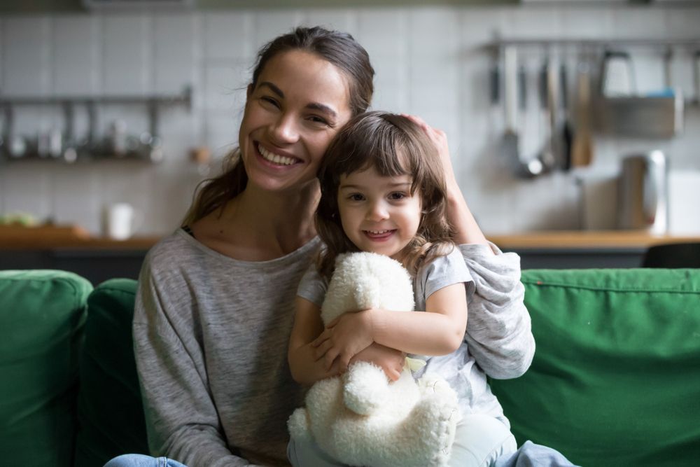 A Woman And A Little Girl Are Sitting On A Couch Holding A Teddy Bear — Bradley J Bragg - Solicitor in Atherton, QLD