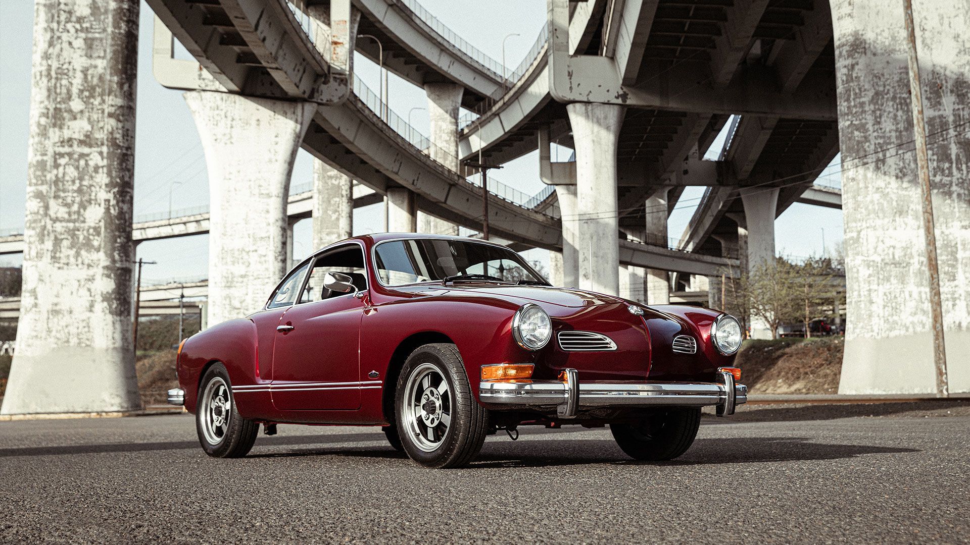 Red vintage car parked under highway overpass.