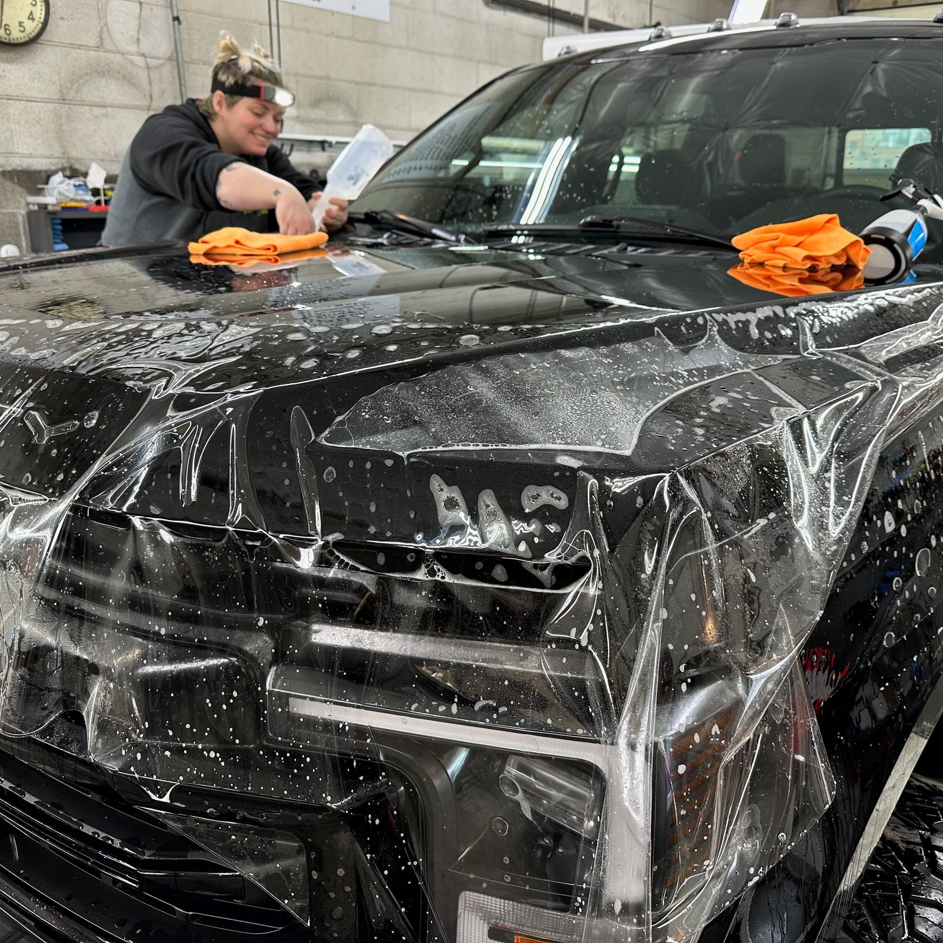 a woman is cleaning the hood of a black truck with a cloth . paint protection film