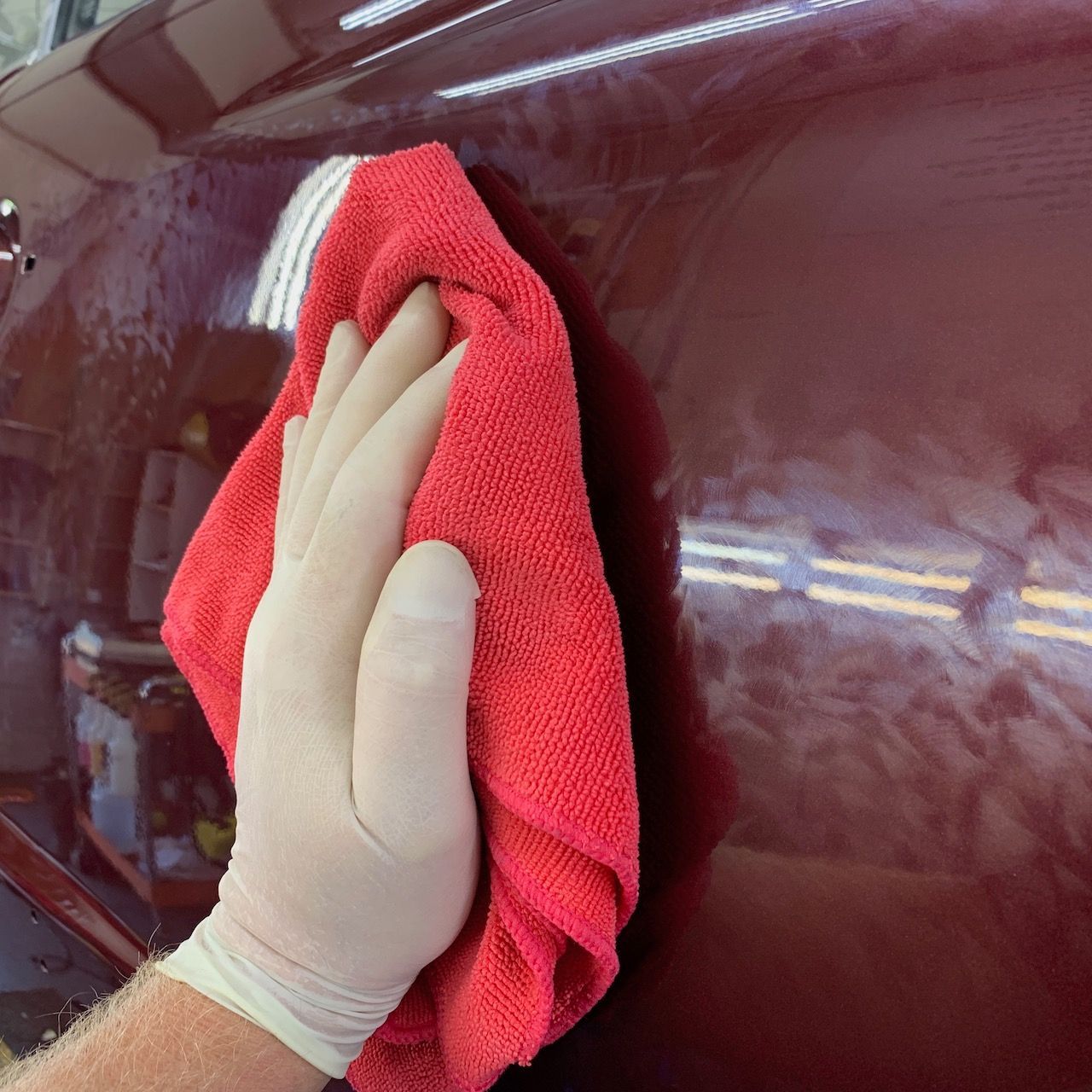 a person wearing gloves is cleaning a red car with a red towel