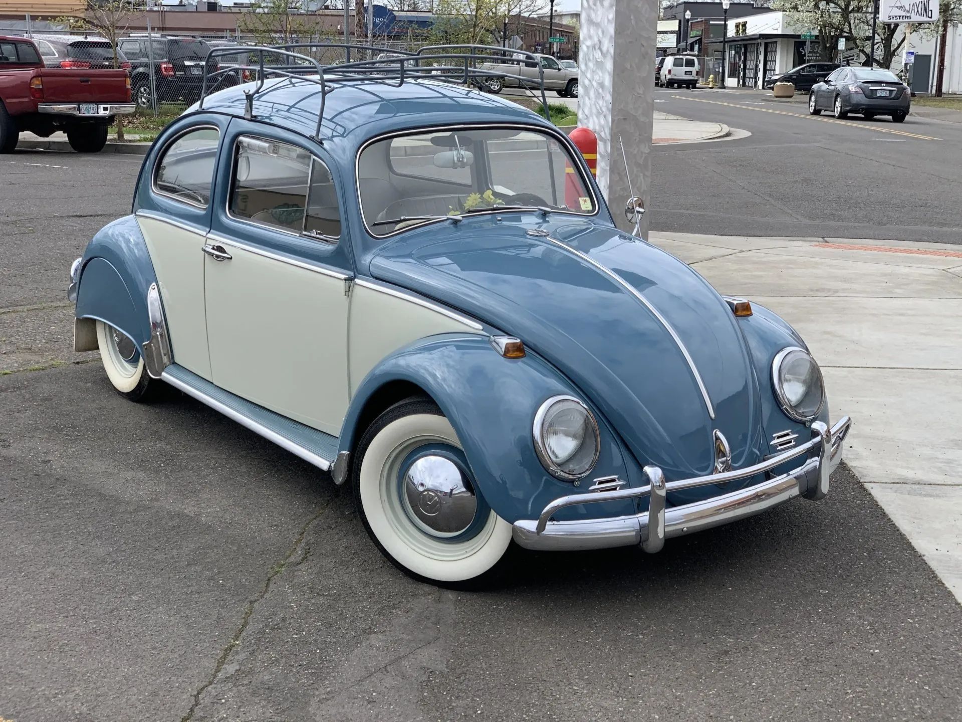 Blue and cream vintage Volkswagen Beetle parked on asphalt in a city setting.